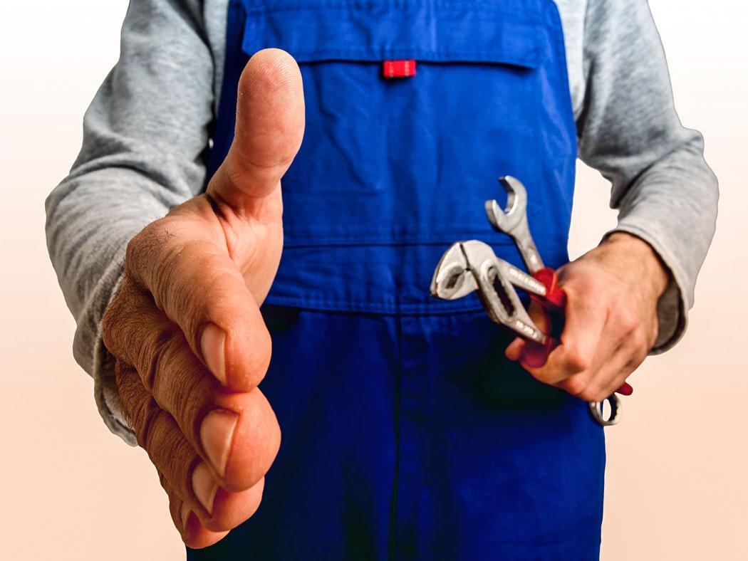 Ein Handwerker in einem Blaumann streckt die Hand zum schütteln aus. 