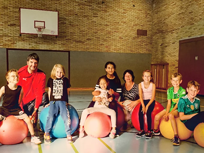 Eine Gruppe von Kindern, die in einer Sporthalle auf Yogabällen sitzt.