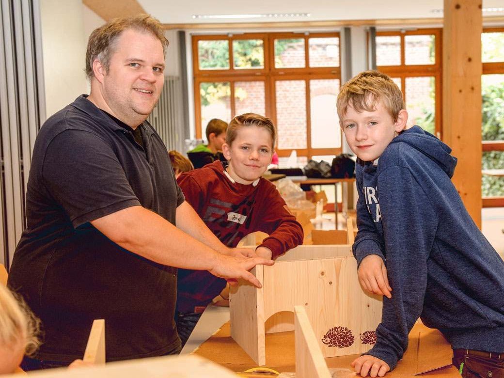 Ein Mann und zwei Jungs sind gerade im Inbegriff eine Holzkonstruktion zusammenzubauen.
