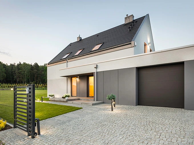 Die Ansicht eines Hauses. Man sieht das Eingangstor, die Haustür, die Garage und den Garten neben dem Haus.