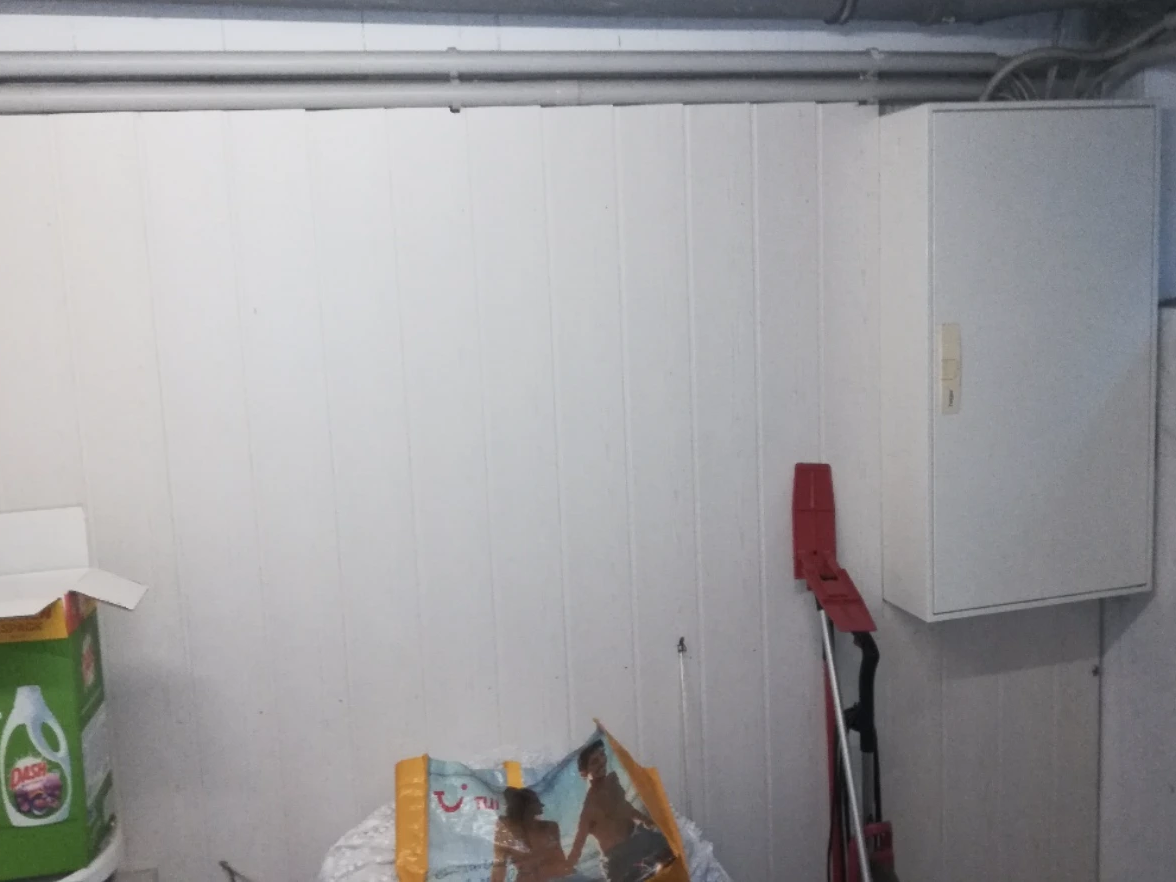 Man sieht einen geschlossenen Stromkasten, der in einem Keller an der Wand hängt.