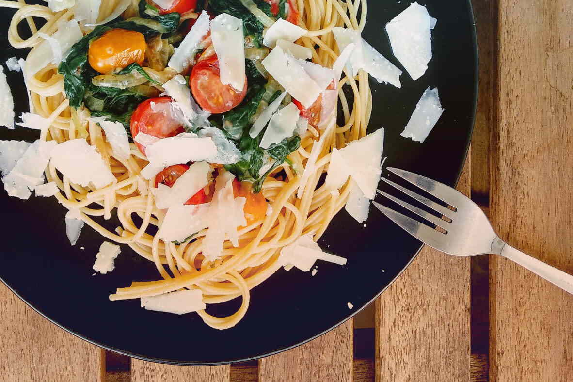 Ein voller Teller Nudeln, mit Tomaten und Parmesankäse ist auf dem Bild zu sehen.