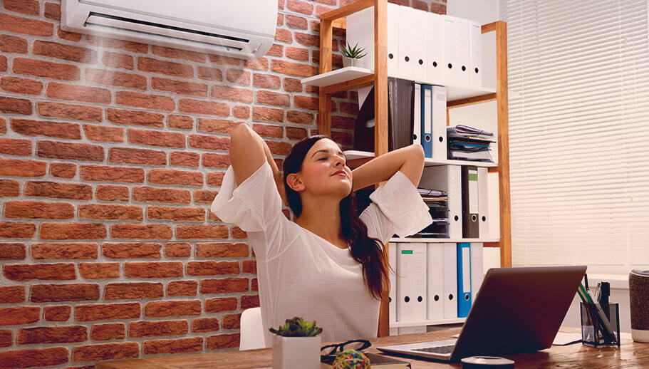 Eine Frau sitzt an ihrem Arbeitsplatz und genießt die Luft aus der Klimaanlage hinter ihr.