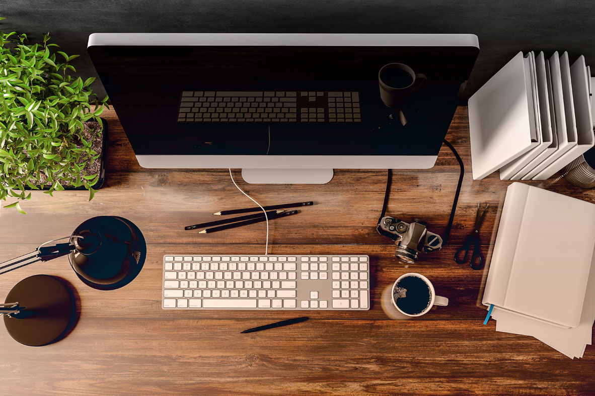 Die Aufnahme eines Arbeitsplatzes aus der Vogelperspektive. Man sieht einen Bildschirm, Tastatur und einen Kaffee.