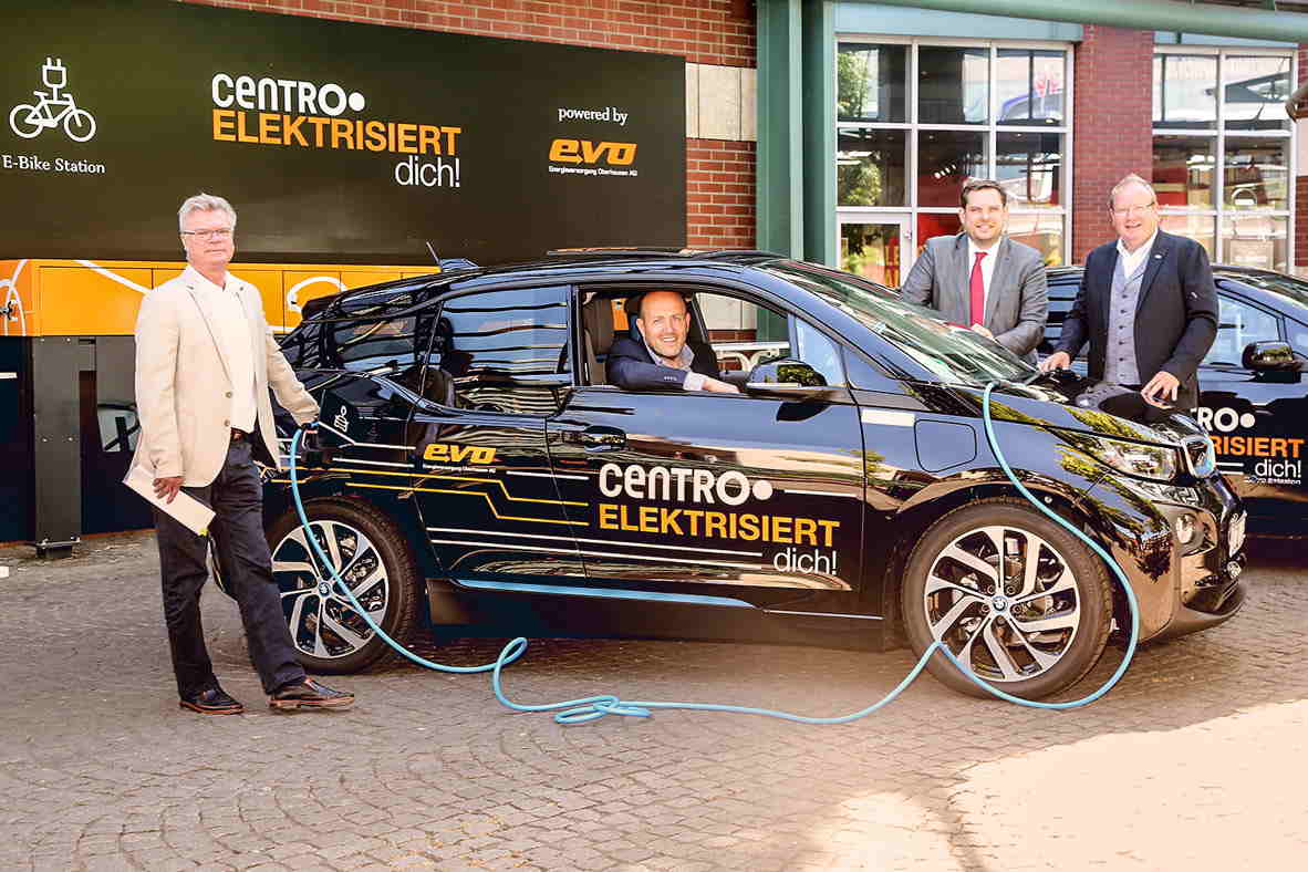 Ein Gruppenfoto neben einem E-Auto. Auf dem Auto ist das evo Logo und der Slogan "Centro elektrisiert dich".