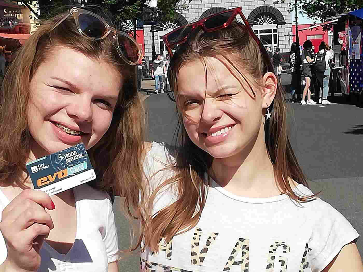 Zwei Mädchen lächeln in die Kamera. Eine von beiden hält unsere evo Kundenkarte in die Kamera.