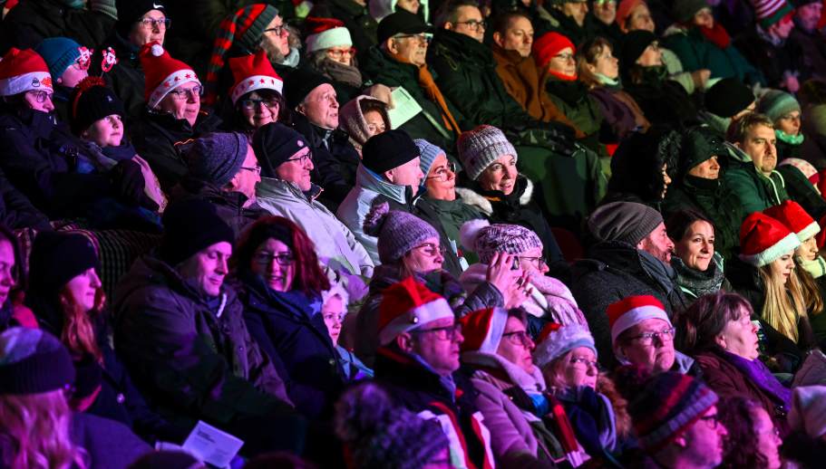 Eine Menge von Menschen mit Weihnachtsmützen, die zusammen singen.